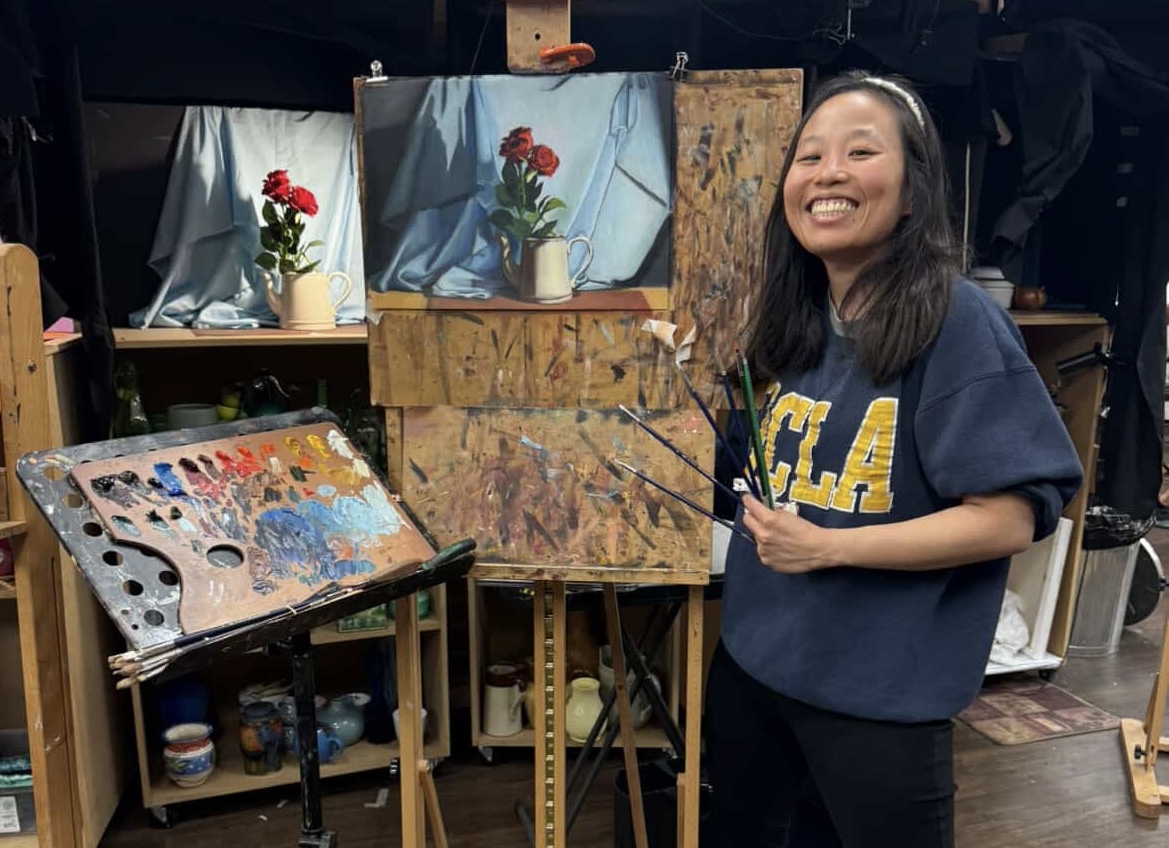 Felicia, live wedding painter, in her studio holding brushes beside an easel and palette
